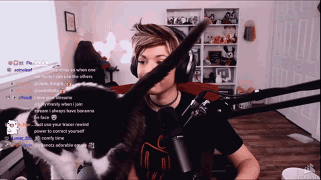 a man wearing headphones is playing with a cat on a twitch channel