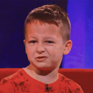 a young boy in a red shirt is making a face