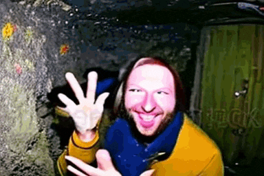 a man with a beard and a yellow shirt is waving his hand in front of a green door .