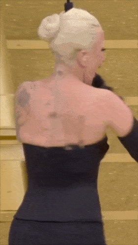 a woman with a tattoo on her back is wearing a black dress and black gloves .