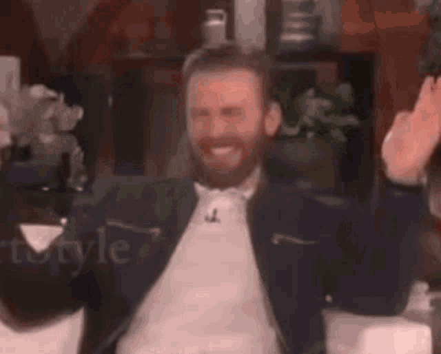 a man with a beard is sitting on a couch with his hands in the air .