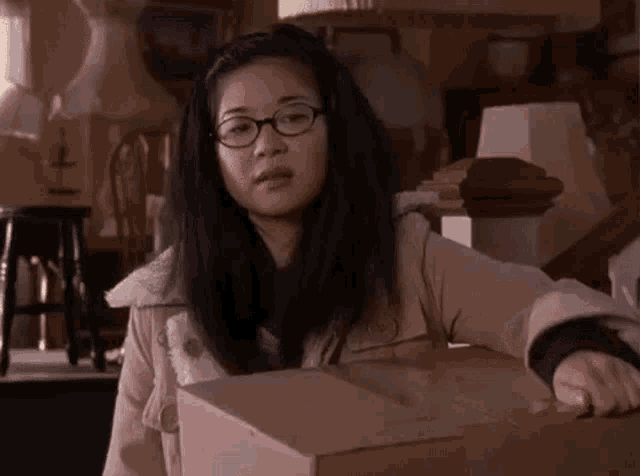 a woman with glasses is holding a cardboard box in a living room .