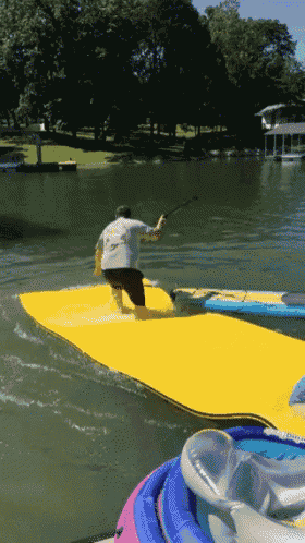 a man in a white shirt is standing on a yellow mat in the water