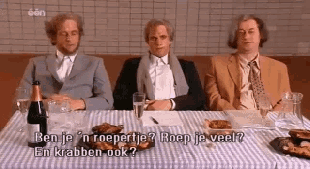three men are sitting at a table with a bottle of champagne and plates of food .