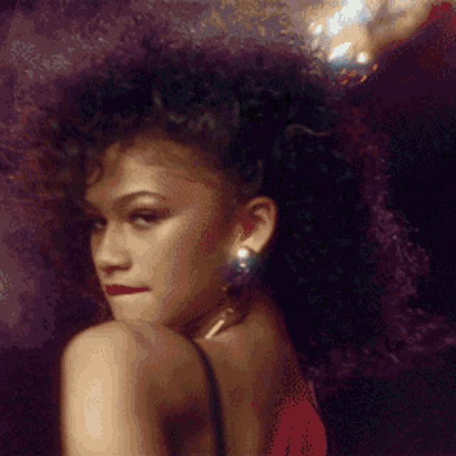 a woman wearing a red dress and earrings looks over her shoulder at the camera