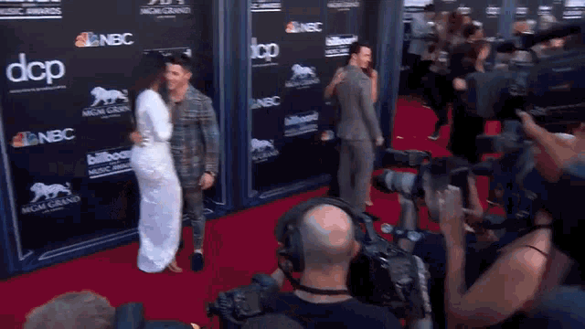 a man and woman are standing on a red carpet in front of a camera .