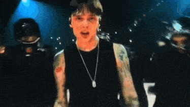 a man with a tattoo on his arm is wearing a black tank top and a necklace .