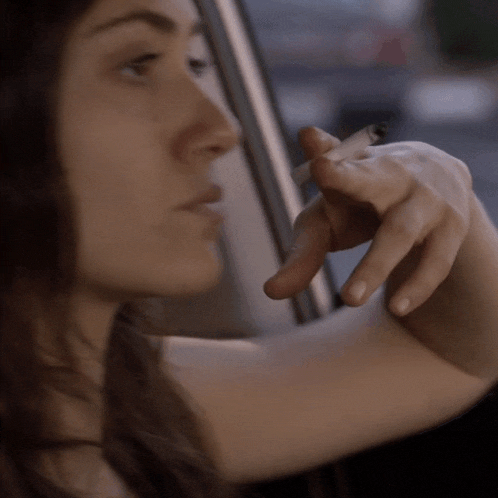 a woman is smoking a cigarette while looking out the window