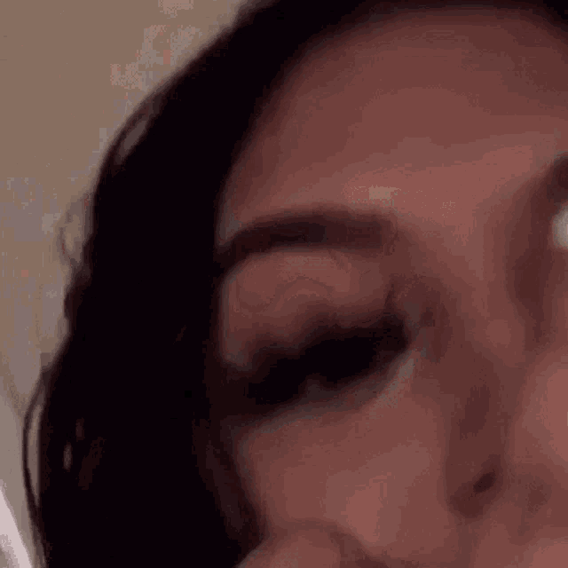 a close up of a woman 's face with her eyes closed and her hand on her face .