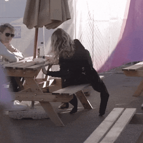 a man and woman sit at a picnic table under an umbrella with a sign that says tm ex in the background