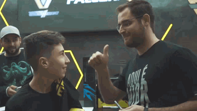 a man wearing a black shirt that says aqui e vibra is talking to another man