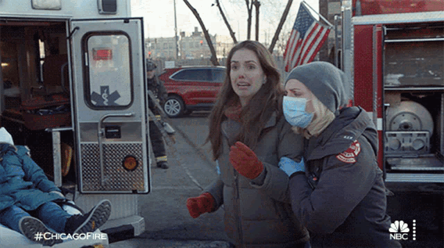a woman wearing a mask is being carried by another woman in front of an ambulance