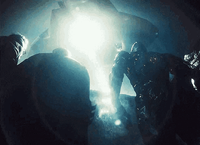 a group of people are standing in a dark room with a light coming out of the ceiling