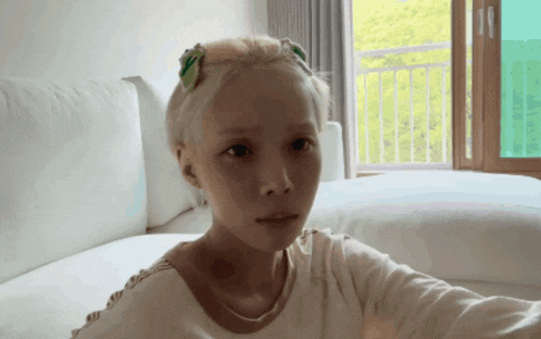 a girl with blonde hair is sitting on a bed and looking at the camera