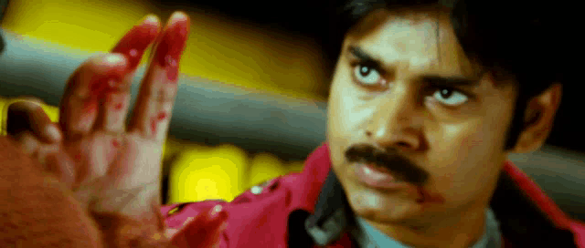 a man with a mustache is holding a bloody hand in front of his face