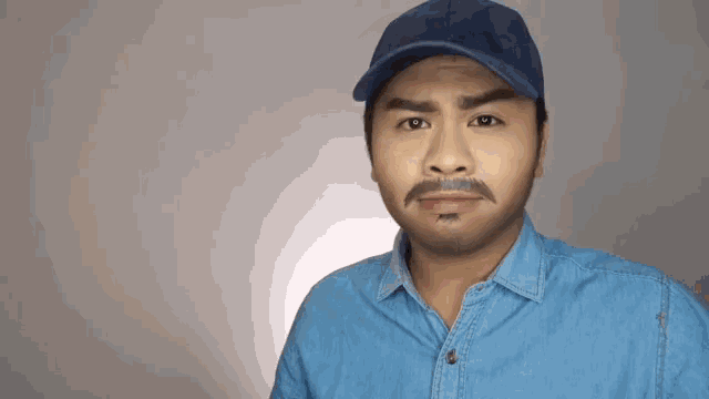 a man wearing a hat and a denim shirt is giving a thumbs up