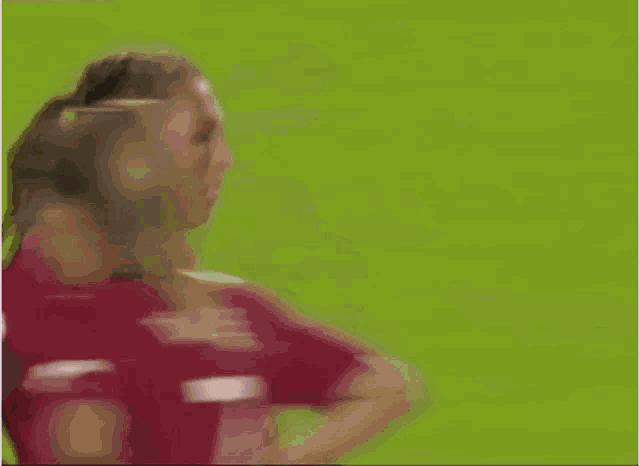 a woman in a ponytail is standing on a soccer field with her head in her hands .
