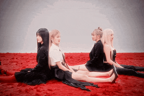 four women are sitting on a red carpet
