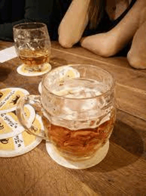 a glass of beer is sitting on a coaster on a wooden table next to a glass of whiskey .