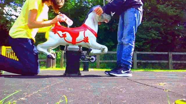 a person is kneeling down next to a rocking horse with a red and white saddle