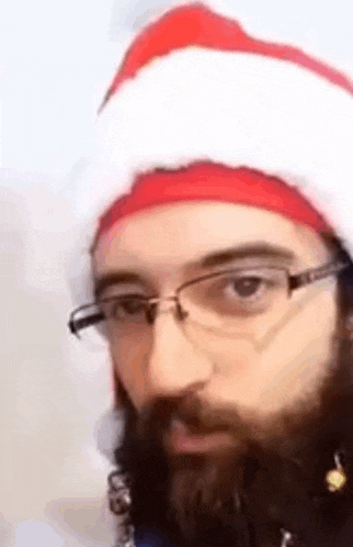 a man with a beard and glasses is wearing a santa hat and earrings .