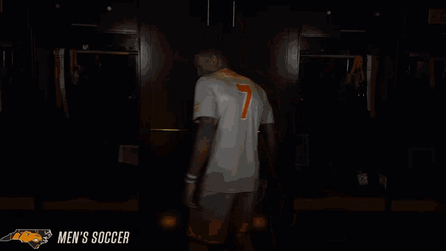 a man stands in a dark room with the words men 's soccer in the corner