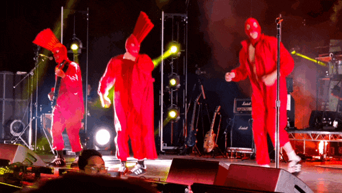 a group of people in red jumpsuits are dancing on a stage in front of a marshall amp