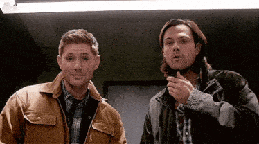 two men in jackets are standing next to each other in a room and looking at the camera .