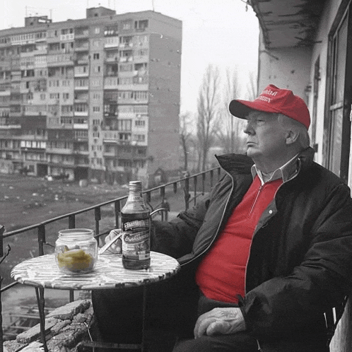 a man sitting on a balcony wearing a red hat that says ' donald trump ' on it