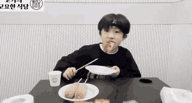 a young boy is sitting at a table eating a hot dog
