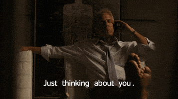 a man sitting on a couch talking on a cell phone with the words just thinking about you above him