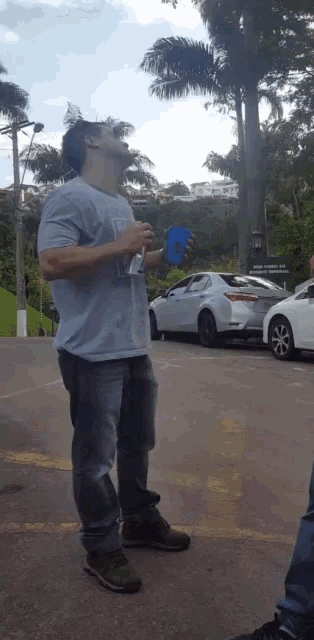 a man in a blue shirt is drinking from a blue cup in a parking lot