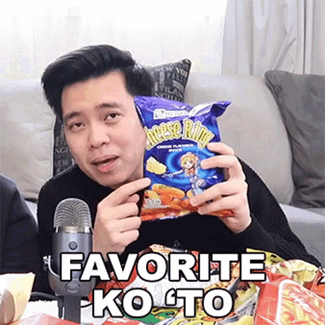 a man is holding a bag of cheese rings in front of a microphone and says favorite ko to