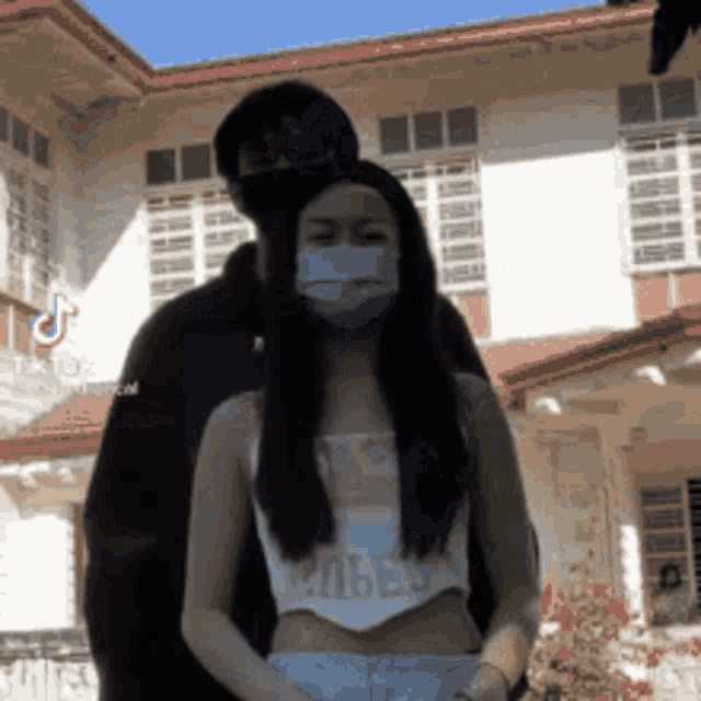a woman wearing a face mask is standing next to a man wearing a mask .