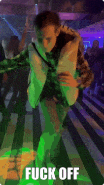 a man in a vest is dancing in a dark room with the words fuck off behind him