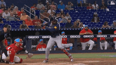 a baseball player swings his bat at a pitch in front of a geico banner