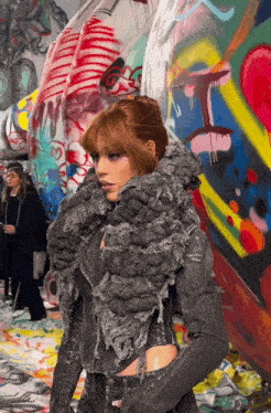 a woman stands in front of a colorful wall with graffiti on it