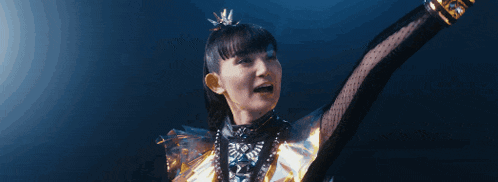 a girl in a metal outfit is dancing with her arms outstretched and making a funny face .