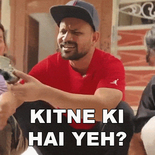 a man wearing a hat and a red shirt is sitting down with a group of people and says kithe ki hai yeh ?