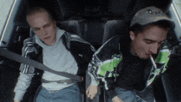 two men are sitting in the back seat of a car one is smoking