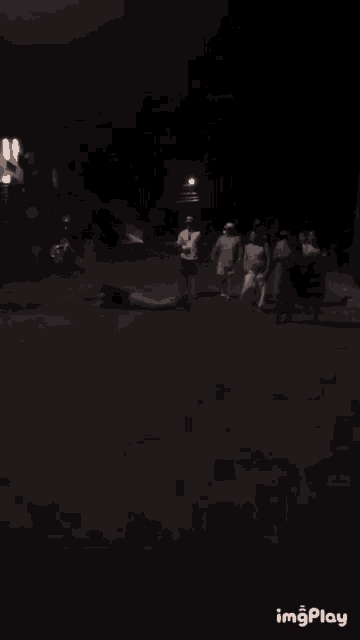 a group of people are walking down a street at night with a person laying on the ground in the middle
