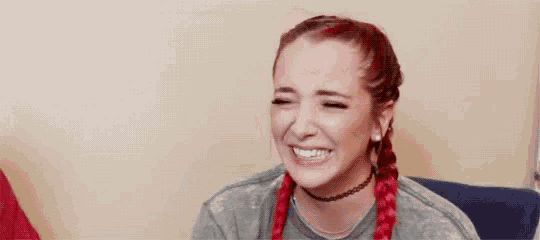 a woman with red braids and a choker is laughing while sitting on a couch .