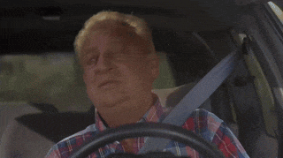 a man in a plaid shirt is driving a car with a seat belt on