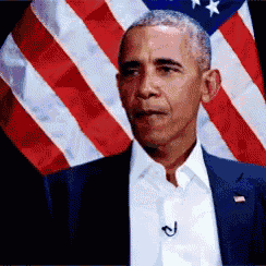 barack obama stands in front of an american flag with a microphone attached to his jacket