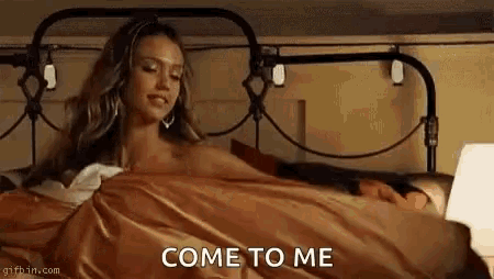 a woman is laying in bed with a laptop and a blanket and says come to me .