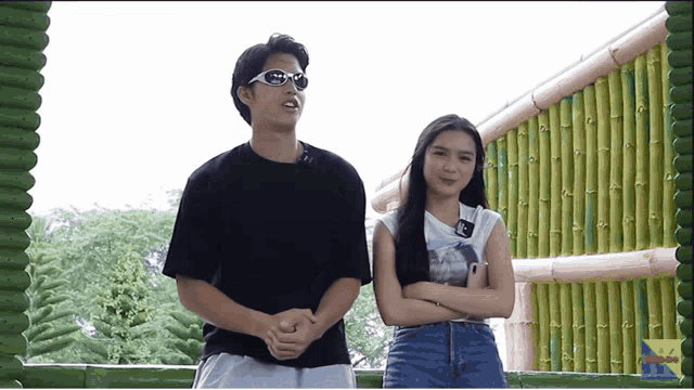 a man and a woman standing next to each other in front of a bamboo wall