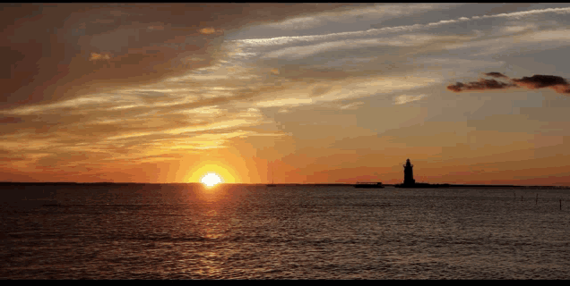 the sun is setting over a body of water with a lighthouse in the distance