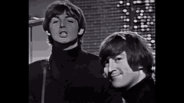 a black and white photo of two men standing next to each other in front of a microphone .