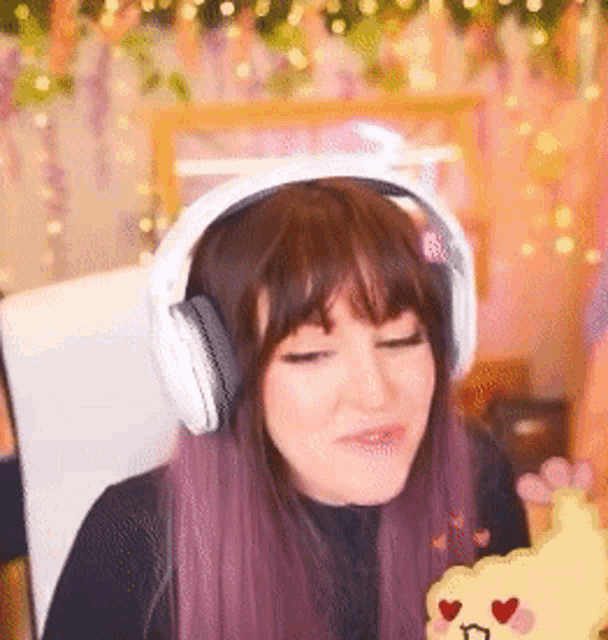 a woman with purple hair is wearing headphones and holding a yellow cloud with hearts on it .