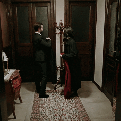 a man in a suit and a woman in a red dress stand in a hallway